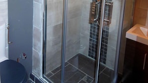 Een douchecabine met glazen wanden, een betegelde muur en een metalen handgreep.