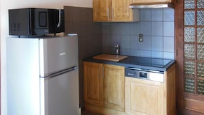 Een compacte keuken met houten kastjes, een witte koelkast, een magnetron, een vaatwasser en een bijzondere kroonluchter.