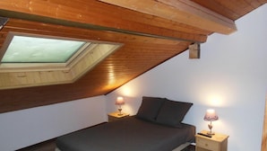 Een slaapkamer met dakraam, een bed, twee nachtkastjes met lampen en een houten vloer.