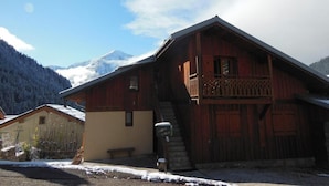 Een houten chalet met balkon, trap en een berg op de achtergrond.