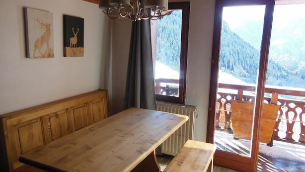 Een houten eettafel met banken, een kroonluchter en uitzicht op een besneeuwde berg door een glazen deur.