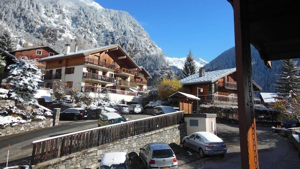 Un albergue de montaña con varios balcones, un estacionamiento con coches y árboles cubiertos de nieve.