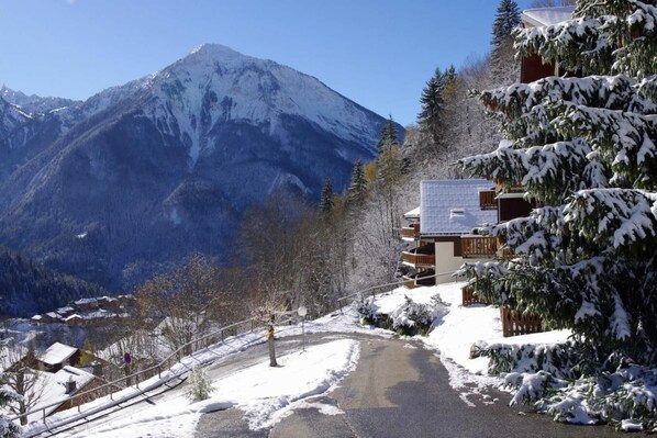A snow-covered mountain with a chalet-style building with a balcony and a ski lift in the foreground.