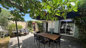 Une terrasse avec une table et des chaises en bois, entourée d’un sol en pierre et de verdure.