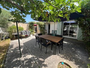Eine Terrasse mit Holztisch und -stühlen, umgeben von Steinplatten und Pflanzen.