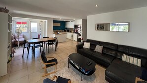 Un salon moderne avec un canapé en cuir noir, une table à manger avec des chaises, un coin cuisine et un petit îlot central doté d’un évier.