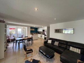 Ein modernes Wohnzimmer mit einem schwarzen Ledersofa, einem Esstisch mit Stühlen, einer Küchenzeile und einer kleinen Kochinsel mit Spüle.