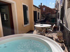 A small outdoor patio with a round table and chairs, a hot tub, and a view of neighboring buildings. - Palazzo Veneziano, located right on Venice's main canal, with a rooftop terrace (Venezia)