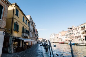 A narrow canal with buildings on either side, a row of boats docked along the water, and a restaurant with outdoor seating at the canal's edge. - Palazzo Veneziano, located right on Venice's main canal, with a rooftop terrace (Venezia)