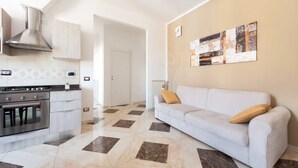 A modern kitchen with a stove, oven, and stainless steel range hood. There is a white sofa with a cushion in a living area with a tiled floor. - 💥💥💥"Marte Suite" -  in the heart of Florence! A/C - WiFi superfast! 💥💥💥 (Firenze)
