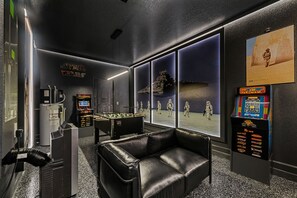 A room with a foosball table, a sofa, Star Wars-themed decor, and a large window with a desert scene.