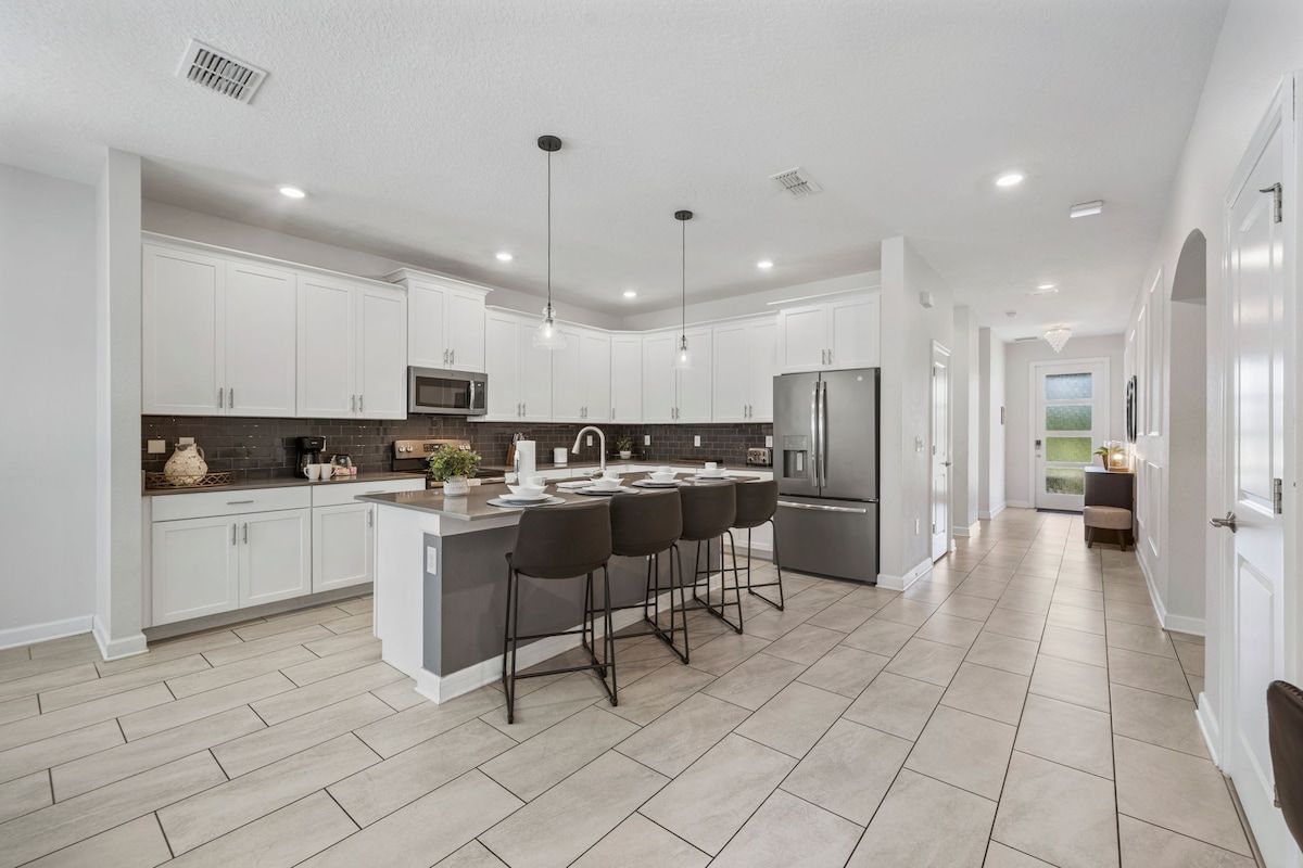 A modern kitchen with white cabinets, a central island with bar stools, and a stainless steel refrigerator.