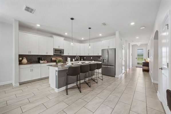 A modern kitchen with white cabinets, a central island with bar stools, and a stainless steel refrigerator.