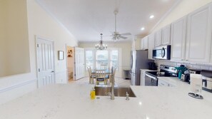 A kitchen with white cabinets, a central island with a sink, a ceiling fan, and a dining area with chairs and a table.