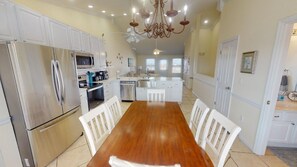 A spacious kitchen with white cabinetry, a wooden dining table, and a stainless steel refrigerator.