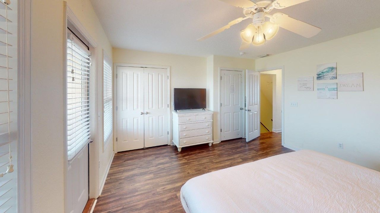 A bedroom with a bed, a dresser, a television, and a ceiling fan.