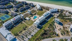 Vista aérea de um resort à beira-mar, com vários edifícios, uma piscina e uma praia.