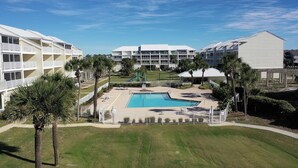 Um hotel com piscina, rodeado por palmeiras e um parquinho.