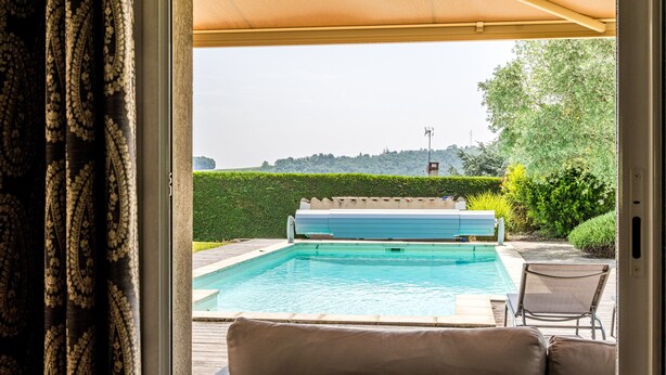 Vista de una piscina con muelle de madera y sillas de descanso, rodeada de follaje y seto.