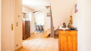 Un pasillo que conduce a un comedor con una escalera, un armario de madera y una estatua de Buda.