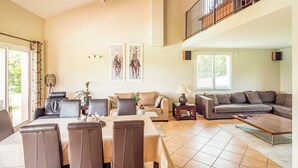 Amplio salón con zona de comedor, escalera a un nivel superior y grandes ventanales que dejan entrar luz natural.