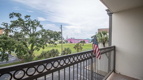 A balcony with a view of a grassy area, trees, and a pink building in the background.