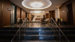 Un vestíbulo de hotel con una escalera monumental, un mostrador de recepción y un candelabro moderno.