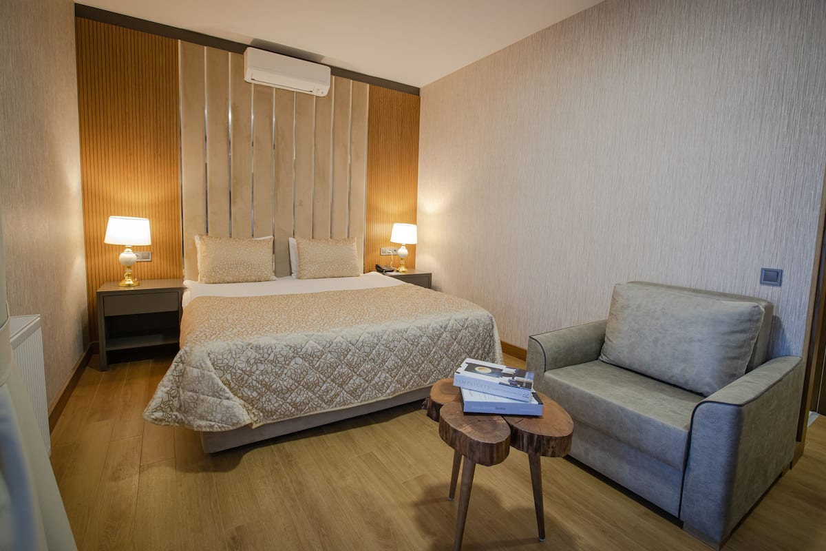 A hotel room with a large bed, two bedside tables with lamps, a grey sofa, and a small wooden table with a book.