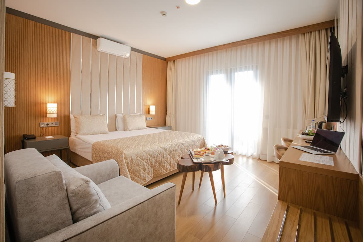 A hotel room with a bed, a sofa, a desk with a laptop, and a tray of breakfast items.