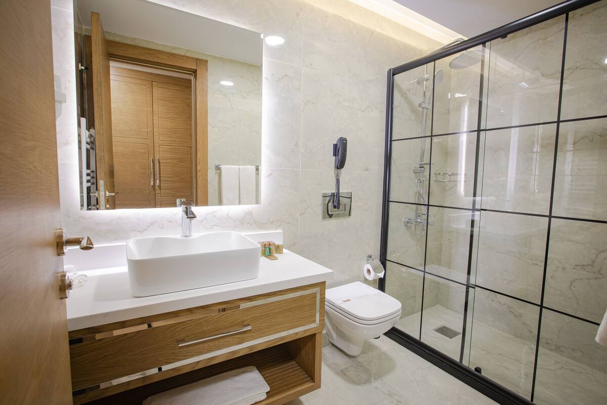 A modern bathroom with a large mirror, a white sink, a toilet, and a glass-enclosed shower area.