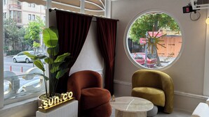 Una sala de estar moderna con una mesa redonda, dos sillones, una planta en maceta y un ventanal con cortinas.