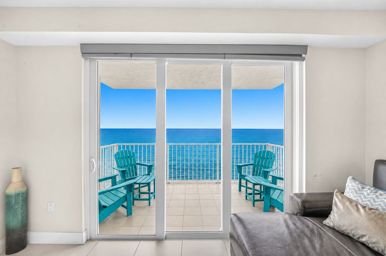 A room with a sliding glass door leading to a balcony with a view of the ocean.