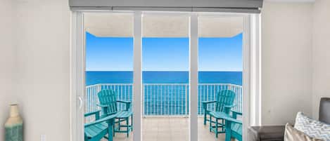 A room with a sliding glass door leading to a balcony with a view of the ocean.