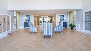 Un hall d’entrée spacieux, doté d’un sol carrelé, de fauteuils à rayures, d’une table ronde et d’une plante en pot.
