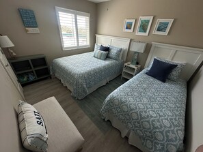 Ein Schlafzimmer mit zwei Betten, einem Fenster, einem Nachttisch und einem an der Wand befestigten Regal.