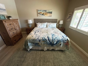 A bedroom with a bed, nightstands, a dresser, and a window with blinds.