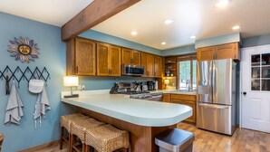 A kitchen with wooden cabinets, a stainless steel refrigerator, and a large island with stools. - PNRD11 - Updated Home, AC, SHARC Passes, Private Hot Tub (Sunriver)