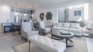 A modern living room with a sofa, armchairs, a coffee table, and a dining area with a kitchen in the background.