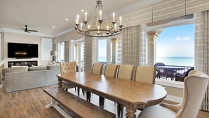 Une salle à manger spacieuse, dotée d’une grande table en bois et de chaises confortables, d’un lustre et offrant une vue sur l’océan.