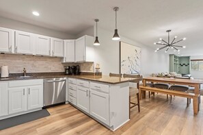 Una cucina moderna con mobili bianchi, un piano di lavoro in legno e un'area pranzo con tavolo e sedie in legno.
