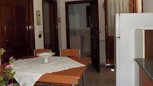 A compact kitchen with a dining table, chairs, a refrigerator, and a door leading to another room. - Mare Natura (Castelsardo)