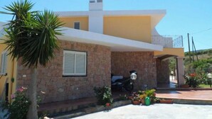 A modern two-story house with a stone facade, a balcony, and a motorbike parked in front. - Mare Natura (Castelsardo)