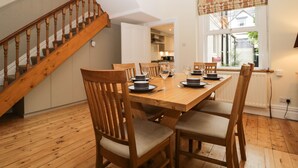 A dining area with a wooden table set for four, surrounded by wooden chairs with cushioned seats. A wooden staircase with a railing is visible to the left. - Shields (Keswick)