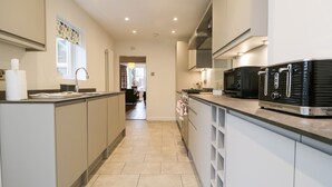 A modern kitchen with a central island, built-in appliances, and a view into the living area. - Shields (Keswick)