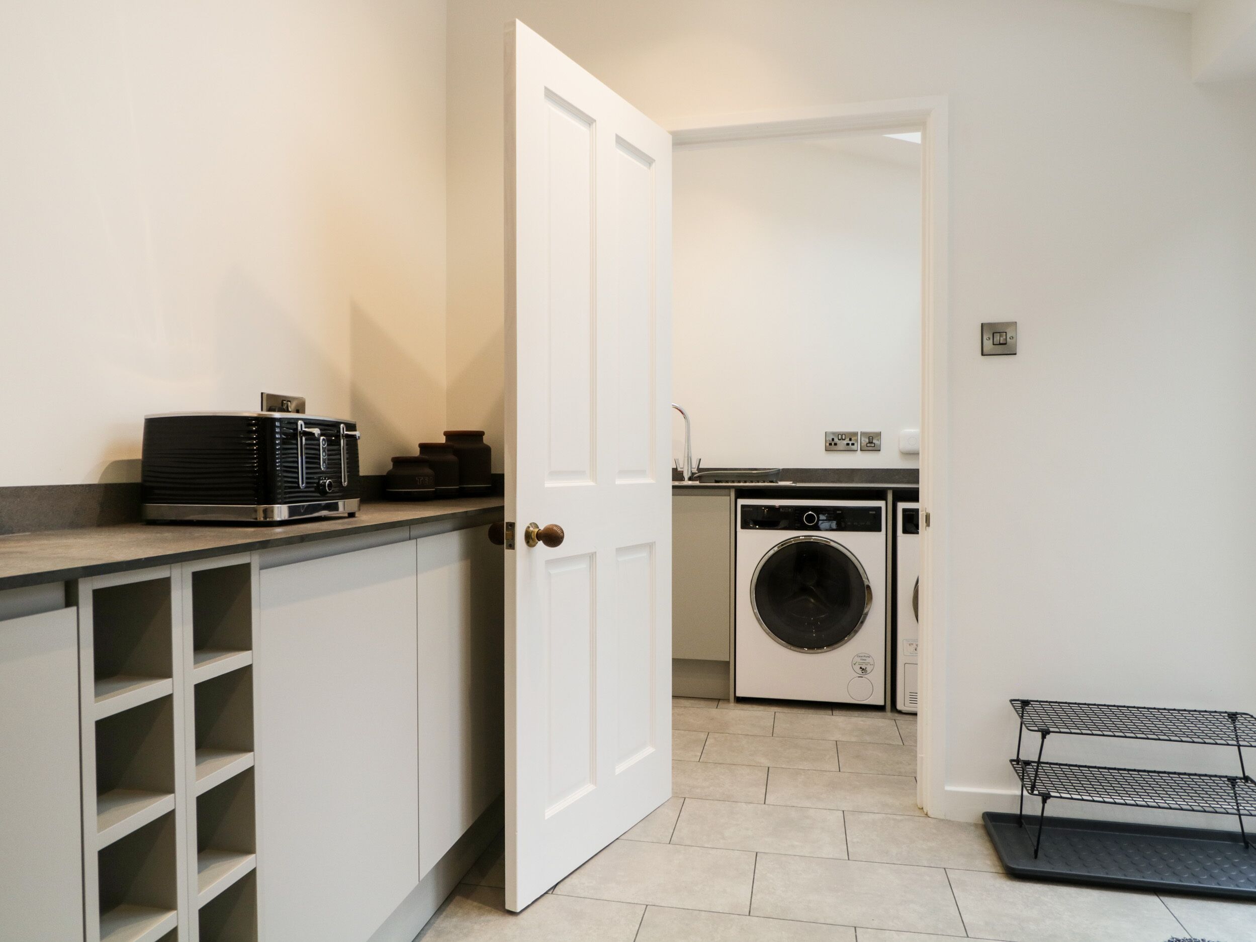 A compact kitchen with a washing machine, a coffee machine, and a metal shelf.