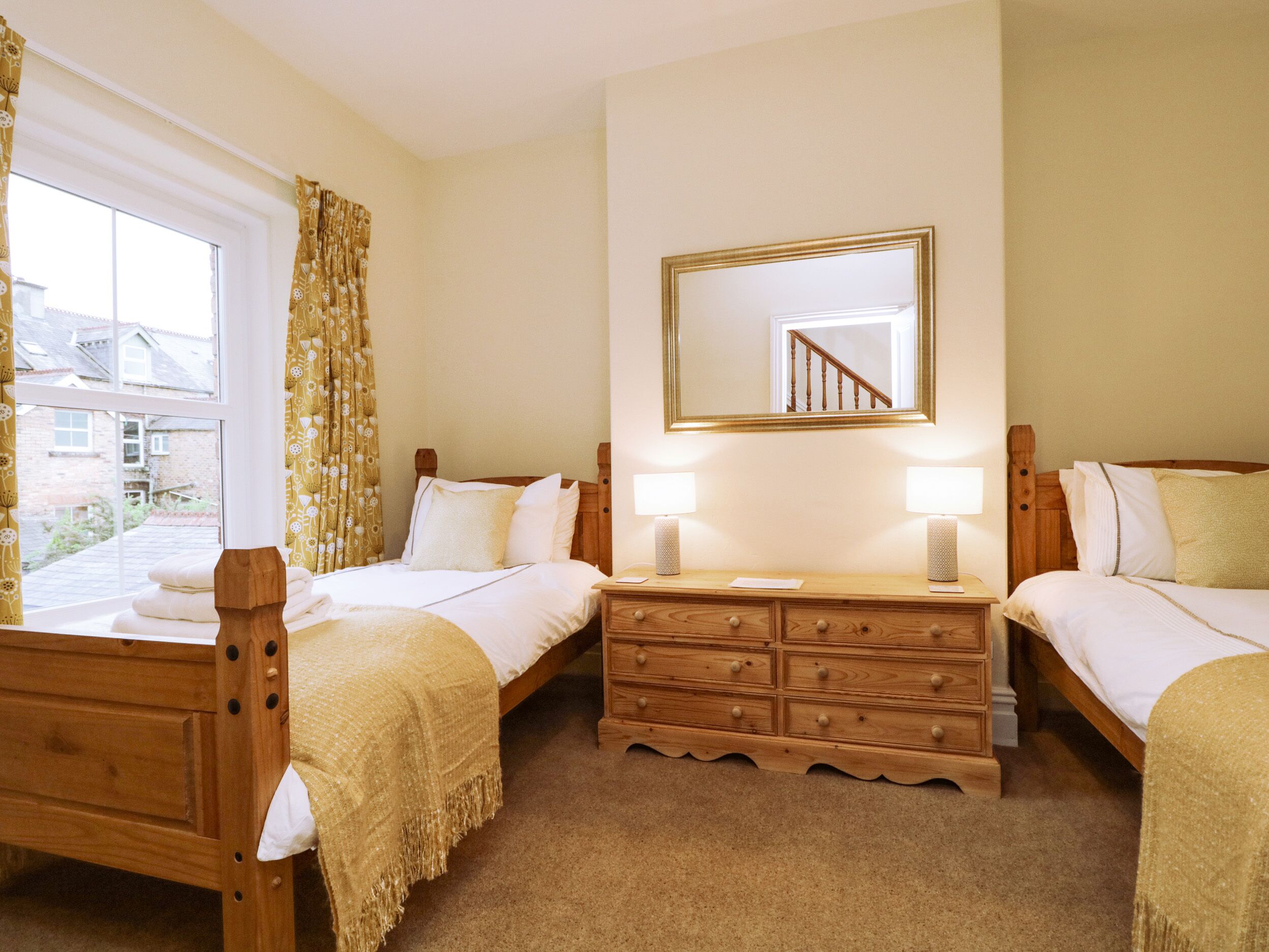 A hotel room with two single beds, a wooden dresser, a mirror, and a window with curtains.