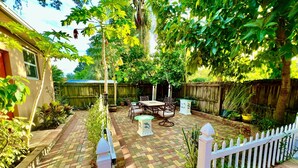 A patio area with a brick floor, outdoor furniture, and a white picket fence.