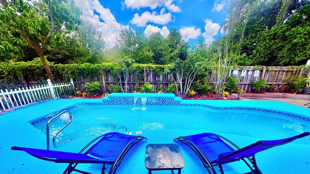 A swimming pool with two lounge chairs and a small table.