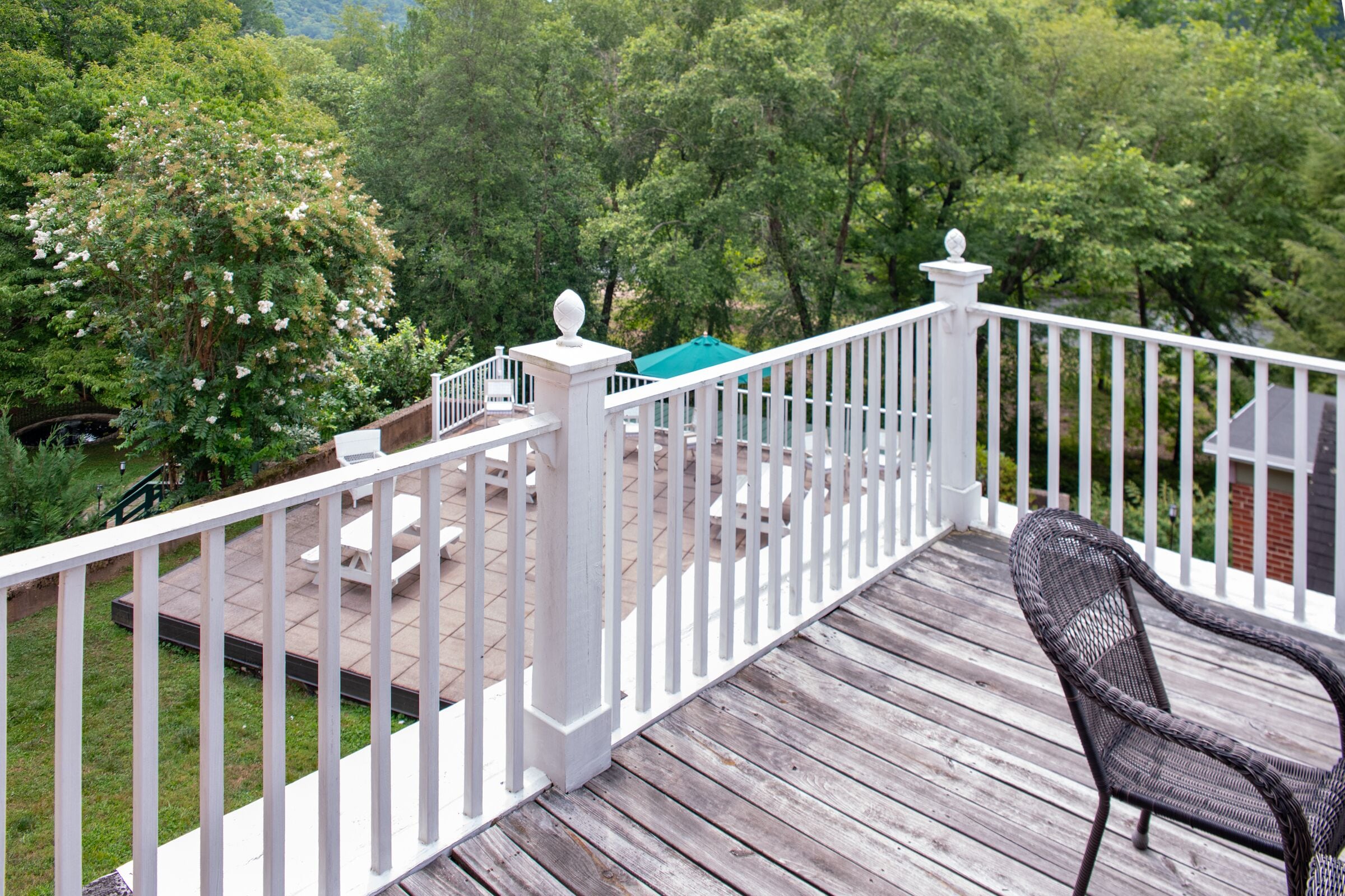 A wooden deck with white railings, a wicker chair, and a green umbrella.