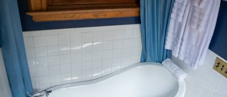 A bathroom with a white bathtub, blue curtains, and a mosaic tile backsplash.